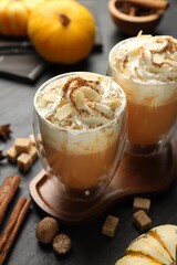Tasty pumpkin latte with whipped cream, spices and fresh vegetables on black table, closeup