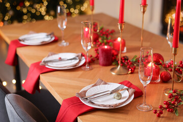 Stylish Christmas table setting with plates, glasses and burning candles in festive decorated room, closeup. Bokeh effect