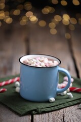 Tasty cocoa with marshmallows and candy canes on wooden table against blurred Christmas lights, closeup. Space for text