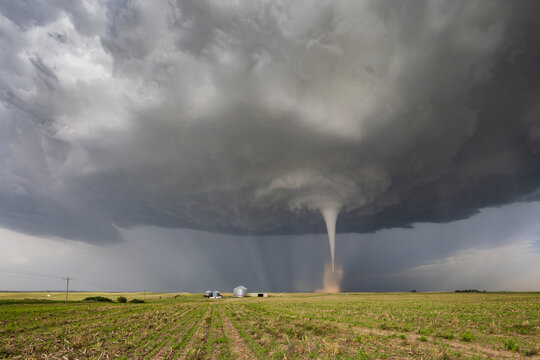 Fully Condensed Tornado, a weather event, clouds and vapour in a whirlwind reaching the ground beside grain elevators. 