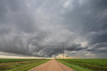 Roll cloud in the sky, a gatheriing storm over a dirt road, reaching to a brighter horizon, 