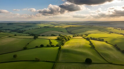 Expansive rolling green hills and patchwork fields bathed in golden hour sunlight under a dramatic sky