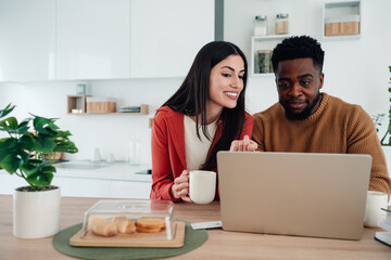 Multiracial couple browsing laptop in modern kitchen