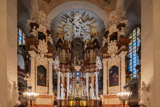 Fototapeta The interior and main altar of St John's Church, in Baroque style, statues and stonework decorations, pillars and carved capitals, paintings and a central cruficix above a gold shrine. 