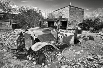 An abandoned classic vintage motor car,  with rusting bent metal, no windows and bare wheel hubs. 