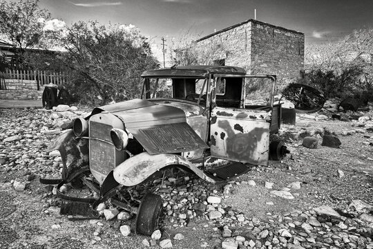 An abandoned classic vintage motor car,  with rusting bent metal, no windows and bare wheel hubs. 