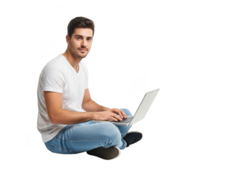 Young man sitting cross legged on the floor working on a laptop computer with a focused expression