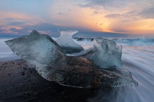 A receding wave and a chunk of calved Ice on the black sand beach at sunset