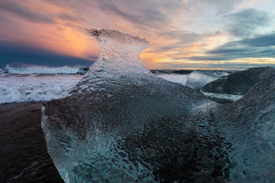 A receding wave and a chunk of calved Ice on the black sand beach at sunset