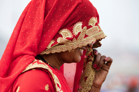 A woman wearing a red sari and head covering decorated with golden thread and flower designs.