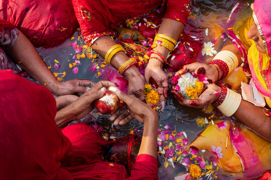 Overhead view of three women wearing bracelets, holding flowers and petals in their henna'ed hands, in water, puja offerings for the gods during the Maha Shivratri Hindu festival.