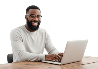 A happy smiling black man with glasses and a beard works on his laptop at a wooden desk looking engaged and productive
