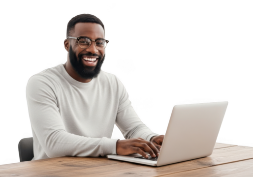 A happy smiling black man with glasses and a beard works on his laptop at a wooden desk looking engaged and productive