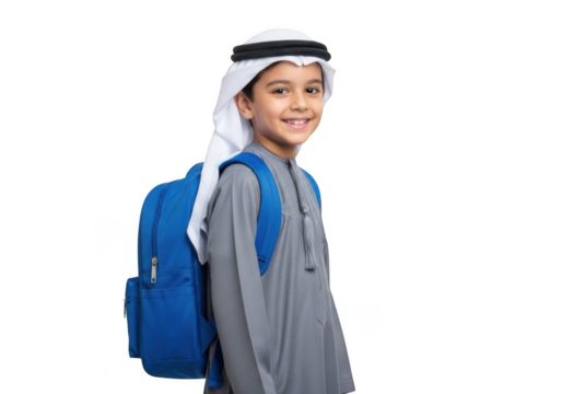 A young boy wearing a traditional white thobe and ghutra carrying a bright blue backpack smiles confidently against a stark black background