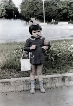 Vintage portrait of a little girl with a toy in her hands in the park. Retro photo from 1972.