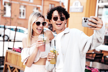 Young smiling beautiful woman and her handsome boyfriend in casual summer clothes. Happy cheerful family. Female having fun. Couple posing in street. Holding and drinking cocktail drink in plastic cup