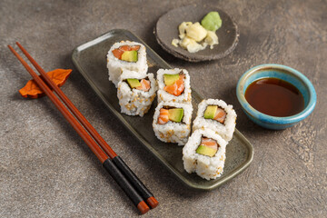California saumon avocat sur table foncée avec sauces soja, baguettes, vaisselle traditionnelle. Cuisine japonaise. 