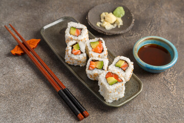 California saumon avocat sur table foncée avec sauces soja, baguettes, vaisselle traditionnelle. Cuisine japonaise. 