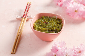 Salade d'algues avec baguettes et décoration fleurs de cerisier sur fond coloré rose