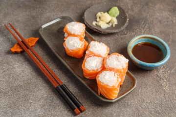 Saumon roll cheese sur table foncée avec sauces soja, baguettes, vaisselle traditionnelle