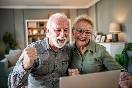 Senior couple celebrating online success using laptop - Powered by Adobe