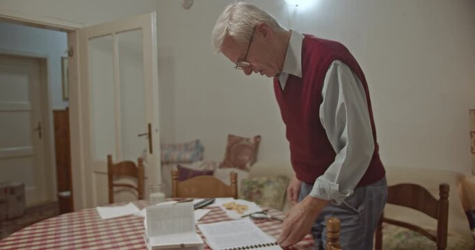 An elderly man in a comfortable home setting gently stretches to alleviate back pain or maintain mobility. He demonstrates a simple routine for senior fitness and well-being.
