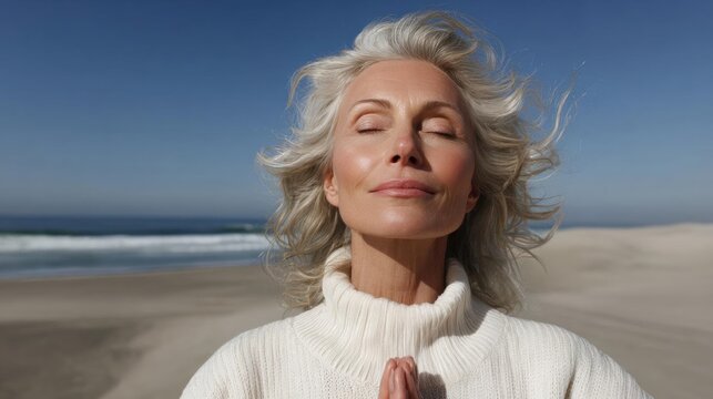 Middle-aged woman with blonde hair, standing on a sandy beach with the ocean in the background.