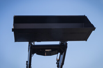 Shovel of excavator or bulldozer on blue sky background. Hydraulic and pneumatic mechanism. Industrial or agricultural machine