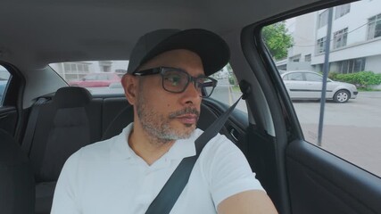 Concentrated man with a beard and glasses driving a car through the city streets