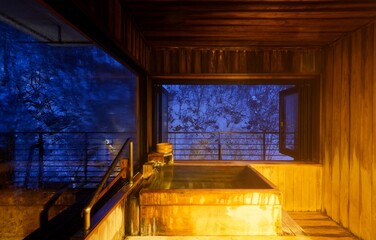 A serene, relaxing winter scene of a private hot spring bath in a traditional Japanese Onsen Ryokan, with vapor rising from the tub and a view of forests on the snowy hillside in Takayama Mura, Nagano