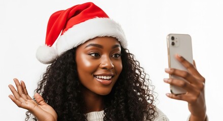 Joyful African American woman in Santa hat, happily making a virtual video call to friends and family, sharing holiday cheer and festive greetings on her smartphone against a clean white background