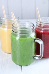 Different tasty smoothies in mason jars on white wooden table