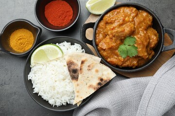 Delicious chicken tikka masala, rice, cilantro, lime, lavash and spices on grey textured table, flat lay