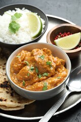 Delicious chicken tikka masala, lavash, cilantro, rice and peppercorns on grey table, closeup