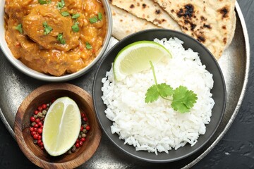 Delicious chicken tikka masala, lavash, cilantro, rice, lime and peppercorns on dark textured table, top view