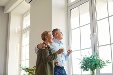Happy senior couple, mature husband and wife standing looking at new frame window in comfortable...