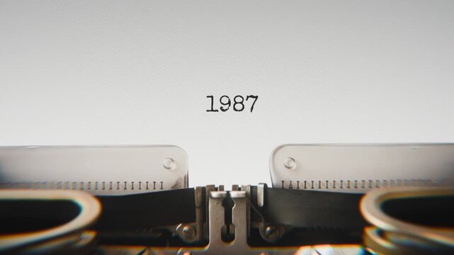Old mechanical typewriter typing Year 1987 in a close-up view, with metal letters striking the white paper.