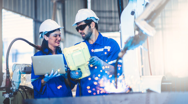 Two engineers mechanic using computer controller Robotic arm for welding steel in steel factory workshop. Industry robot programming software for automated manufacturing technology