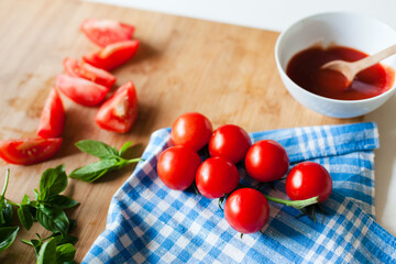 Cherry tomatoes, fresh basil on wooden cutting board, home cooking. Organic sauce, eco-friendly vegetables, healthy ingredients. Local grown, natural food and lifestyle. Sustainable, mindful eating