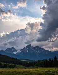 Fototapeta premium Majestic mountain range under dramatic storm clouds and sunlight.