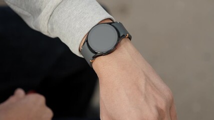 Close up of person wearing new stylish and functional for daily use smartwatch while sitting outside. Modern trendy black round smartwatches on male hand outdoors.
