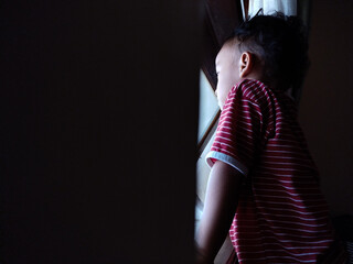 Young child gazing out a window with gentle lighting creating a peaceful indoor atmosphere
