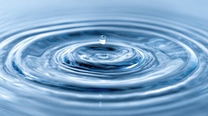 A drop of water falls into a tranquil surface producing beautiful circular ripples as it splashes.