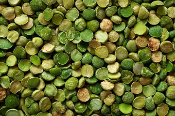 Close-up of dried green split peas scattered on a surface. The peas vary in shades of green, showcasing their natural texture and color variations.