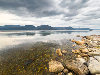 Calm crystal clear water reflecting mountains in northern norway under a cloudy sky