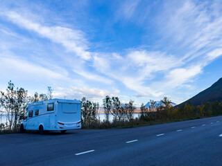 Motorhome driving on a scenic road in Kiruna, Sweden, with autumn foliage and beautiful lake views.