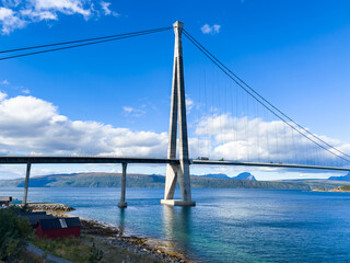 Cars driving on helgeland bridge over a fjord in norway, with mountains and blue sky in the background