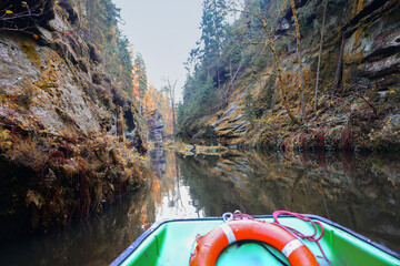 Autumn river journey in a quiet canyon, green boat with lifebuoy in tranquil nature scene.