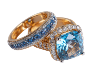 Two gold rings, featuring a large, square, light-blue gemstone,  surrounded by smaller,  light-blue gemstones and diamonds,  rest atop each other