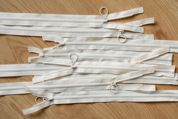 numerous beige zippers arranged on a wooden surface, viewed from above